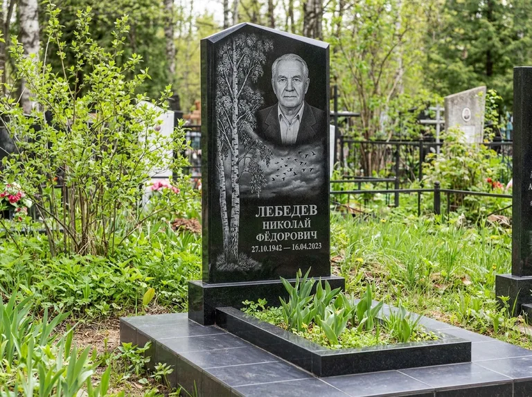 Памятник с гравировкой берёзы: вертикальная стела со скошенным верхом — берёза и стая птиц в небе, гранитный цоколь с тёмной плиткой, работа «Лебедев» в Новом Уренгое