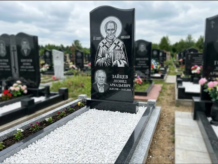 Памятник с гравировкой иконы: стела с крестообразным навершием — икона в резной рамке-киоте, газон без ограды, стриженая трава, работа «Раевская» в Новом Уренгое
