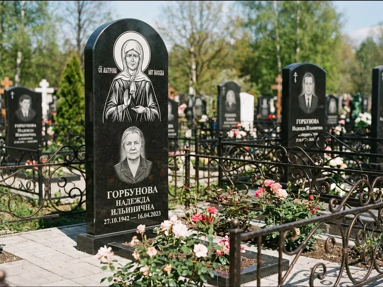 Памятник с гравировкой иконы: стела с арочным верхом и киотом под образ — гравировка образа Матроны Московской, гранитный цоколь с тёмной плиткой, работа «Ковалёв» в Новом Уренгое