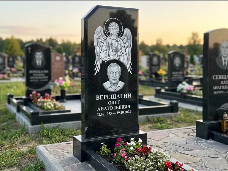 Памятник с гравировкой иконы: стела с резным навершием и нимбом в золоте — гравировка образа Спасителя, высокие разросшиеся туи полукругом, работа «Мельникова» в Новом Уренгое