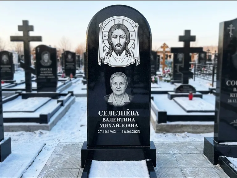 Памятник с гравировкой иконы: небольшая скромная одиночная стела с именной иконой — золочёный нимб на образе, аккуратный участок с газоном, работа «Ковалёв» в Новом Уренгое