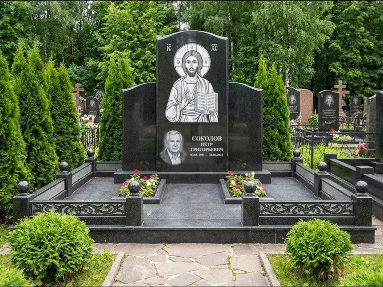 Памятник с гравировкой иконы: широкая горизонтальная лежачая плита-стела — икона в резной рамке-киоте, серая гравийная отсыпка с бордюром, работа «Богданова» в Новом Уренгое