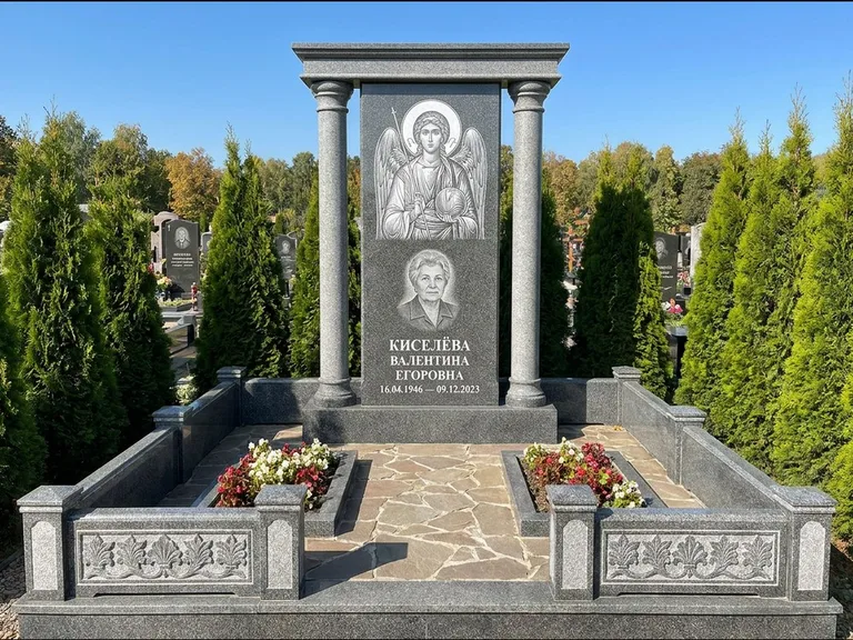 Памятник с гравировкой иконы: массивная стела с двускатным навершием-домиком — гравировка Николая Чудотворца, живая изгородь из туи, работа «Журавлёв» в Новом Уренгое