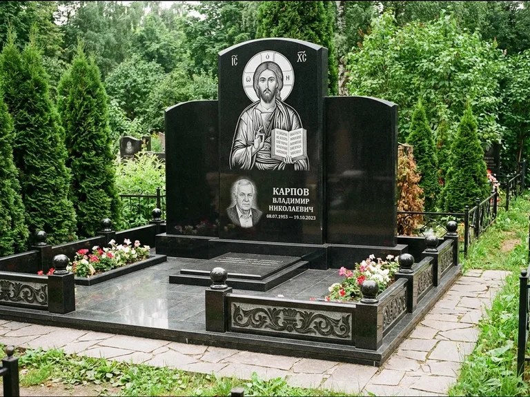 Памятник с гравировкой иконы: широкая панорамная стела с золочёным нимбом — гравировка образа Матроны Московской, цветник с белыми хризантемами, работа «Мельникова» в Новом Уренгое