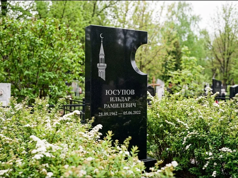 Мусульманский памятник с гравировкой мечети: стела с боковым вырезом в форме полумесяца — гравировка минарета с полумесяцем, низкие кусты спиреи в цвету, работа «Юсупов» в Новом Уренгое