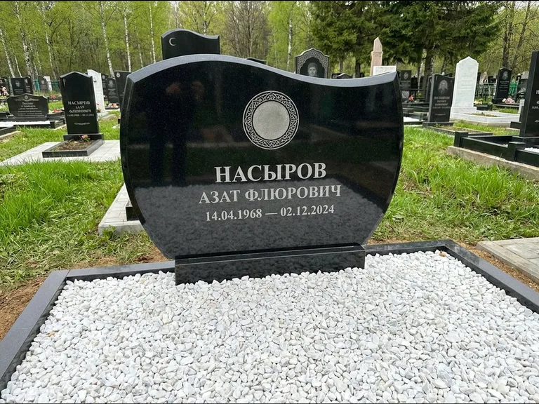 Мусульманский памятник: стела с волнообразным скошенным верхом — гравировка мечети под полумесяцем и звёздами, белая мраморная крошка с бордюром, работа «Насыров» в Новом Уренгое