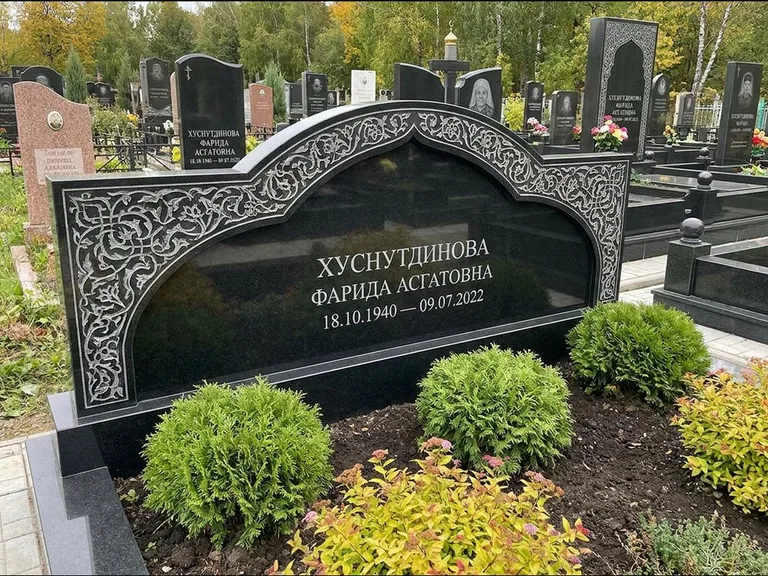 Мусульманский памятник: вытянутая горизонтальная семейная стела с аркой — белая гравировка силуэта мечети с минаретами, участок с декоративными кустами, работа «Зарипова» в Новом Уренгое
