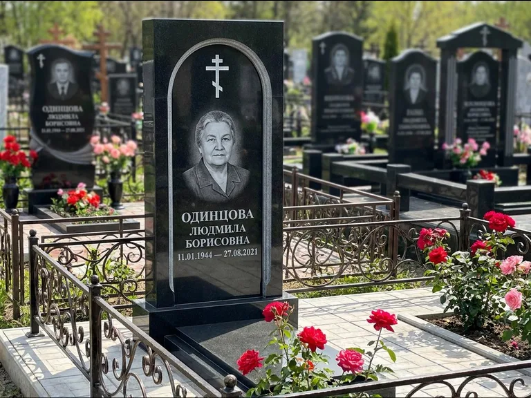 Памятник из чёрного гранита — скромная невысокая стела с крестом с терновым венцом, работа «Лаврентьева» в Новом Уренгое